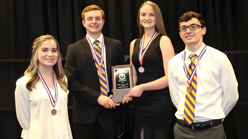 Vier Schülerinnen und Schüler der Scottsburg High School stehen gemeinsam auf einer Bühne und halten Auszeichnungen und Medaillen.