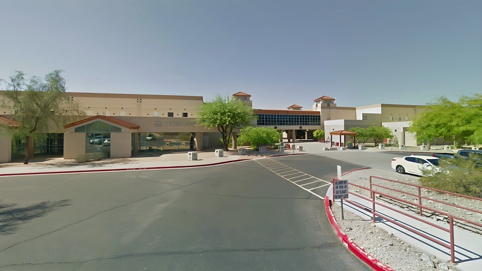 Ein Schulgebäude des Scottsdale Unified School District mit Parkplatz und Bäumen im Vordergrund unter klarem blauem Himmel.