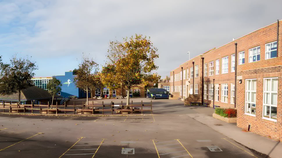 Das Backsteingebäude der Seaford Head School mit einem Hof und bunt gefärbten Herbstbäumen unter einem wolkigen Himmel.