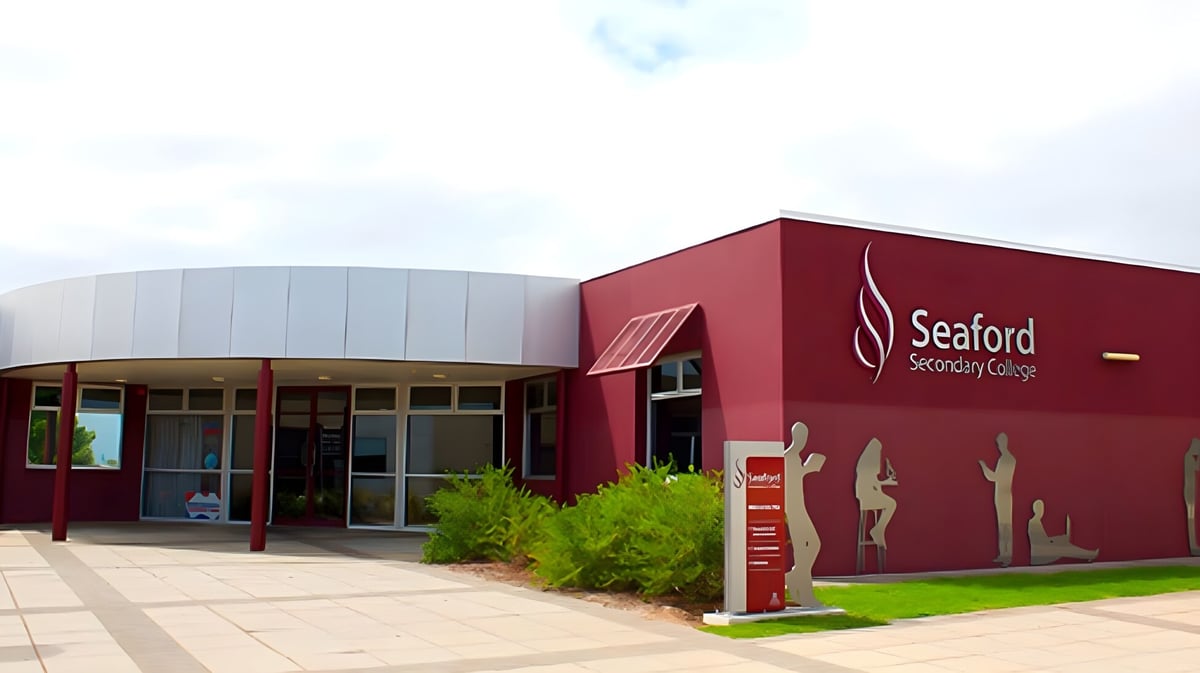 Das moderne rote Gebäude mit dem Logo des Seaford Secondary College steht auf einem grasbedeckten Gelände unter bewölktem Himmel.