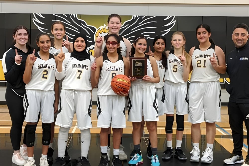Eine Gruppe weiblicher Basketballspielerinnen der Seaquam Secondary School hält in der Turnhalle einen Pokal.