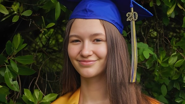 Eine junge Frau mit blauer Abschlussmütze lächelt im grünen Freien auf dem Campus der Seattle Public Schools.