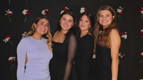 Vier Schülerinnen mit langen dunklen Haaren stehen vor einem schwarzen Hintergrund mit roten und weißen Blumenmustern auf dem Campus der Seattle Public Schools.