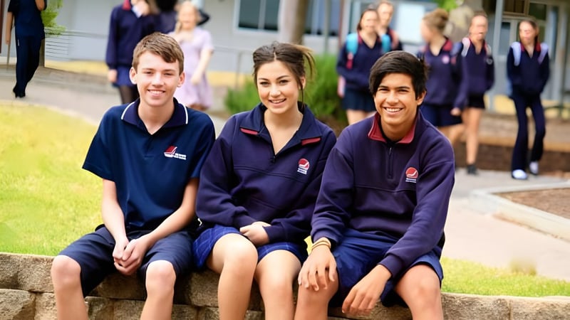 Drei Schüler sitzen gemeinsam auf einer Steinmauer vor dem Schulgebäude der Seaview High School.