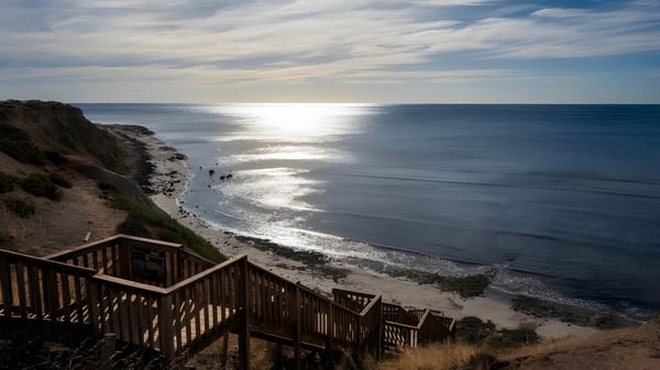 Eine Holztreppe führt zum Strand mit sanften Wellen unter bewölktem Himmel auf dem Gelände der Seaview High School.