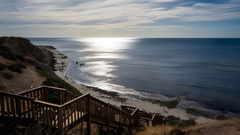 Eine Holztreppe führt zum Strand mit sanften Wellen unter bewölktem Himmel auf dem Gelände der Seaview High School.
