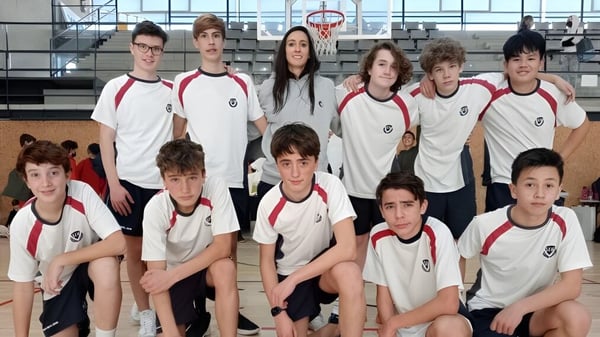 Eine Gruppe von Schülerinnen und Schülern der SEK International School Catalunya posiert in einer Sportarena mit Basketballkorb im Hintergrund.