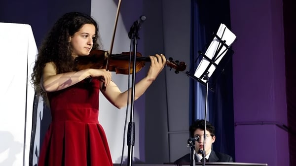 Eine Schülerin der SEK International School El Castillo spielt im roten Kleid Violine auf der Bühne.