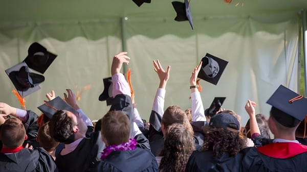 Eine Gruppe von Absolventen der SEK International School El Castillo wirft ihre Abschlusskappen vor grünen Vorhängen in die Luft.
