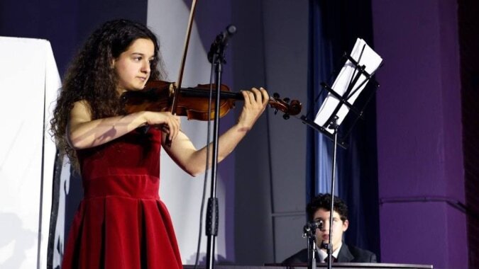 Eine Schülerin der SEK International School El Castillo spielt Violine auf der Bühne während ein Mann im Hintergrund steht.