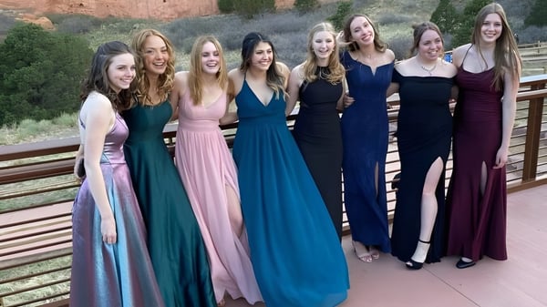 Eine Gruppe Schülerinnen der Semiahmoo Secondary School steht in bunten formellen Kleidern auf einem Holzdeck mit natürlicher Landschaft im Hintergrund.