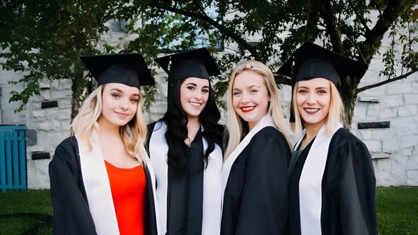 Vier Absolventinnen des Séminaire de Chicoutimi posieren gemeinsam vor einem bewaldeten Hintergrund.