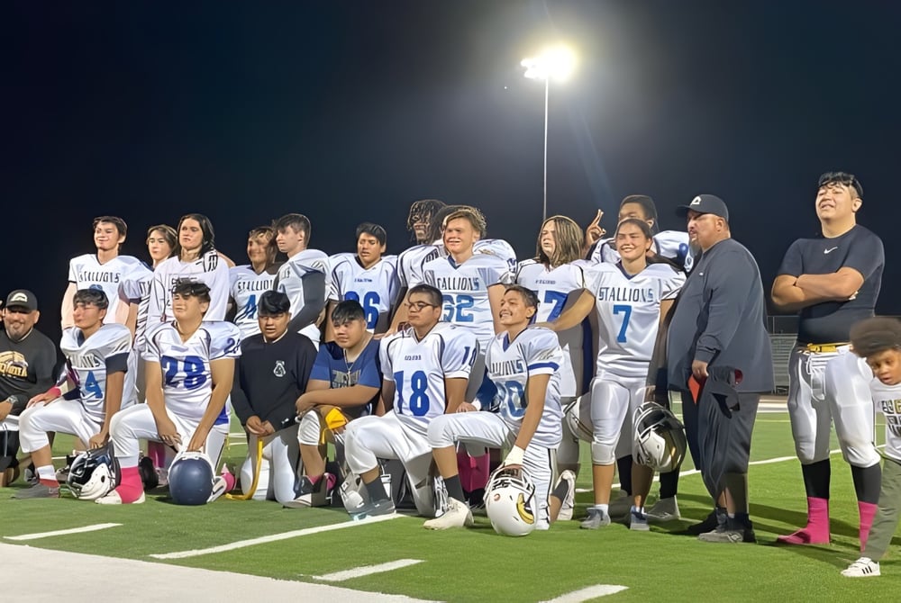 Eine Gruppe junger Fußballspielerinnen und Fußballspieler posiert nachts auf dem beleuchteten Fußballfeld der Sequoia Charter High School.