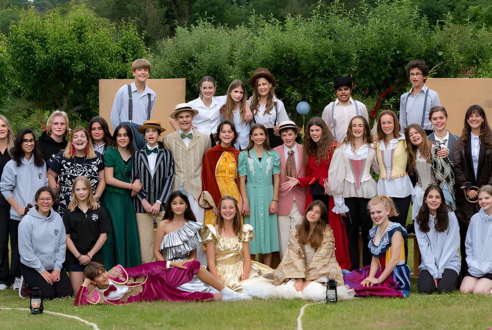 Eine Gruppe von Schülerinnen und Schülern der Sevenoaks School steht draußen vor grüner Landschaft.