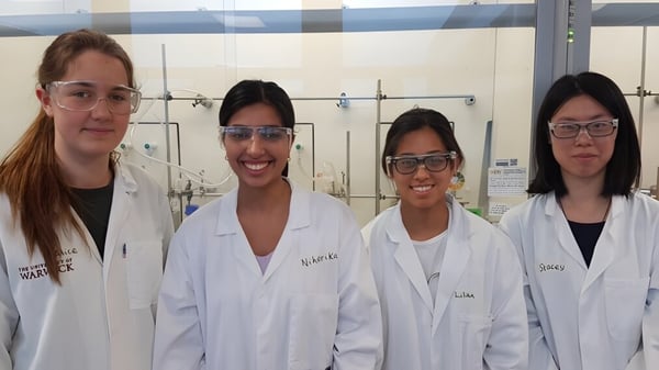 Vier Schülerinnen und Schüler der Sevenoaks School stehen in weißen Laborkitteln in einem Labor mit wissenschaftlichen Geräten.