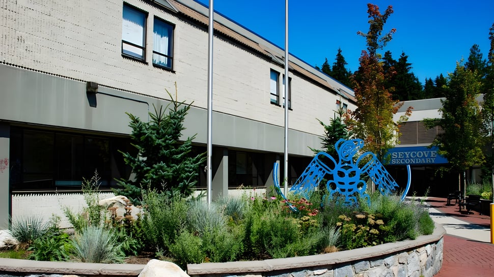 Das moderne Gebäude der Seycove Secondary School mit einer blauen Skulptur und gepflegtem Garten im Vordergrund.