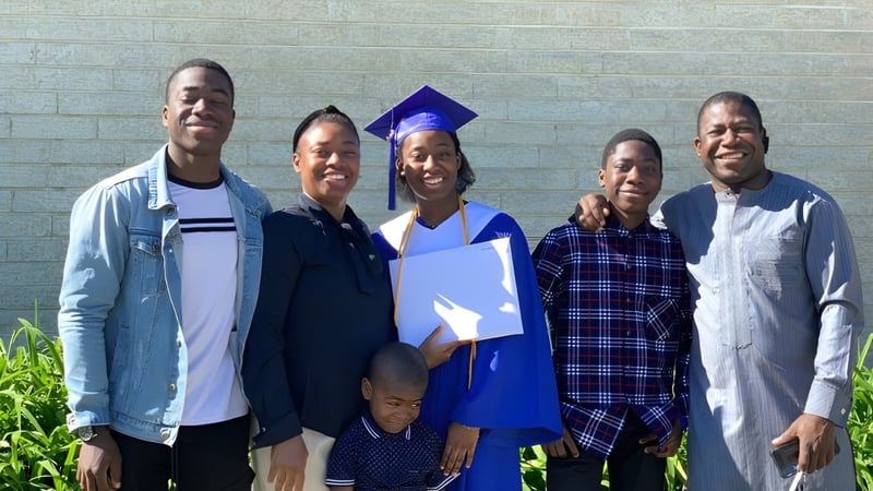 Eine Gruppe von Schülerinnen und Schülern, darunter eine Person in einer Abschlussrobe, vor einer Backsteinwand auf dem Campus der Shaftesbury High.