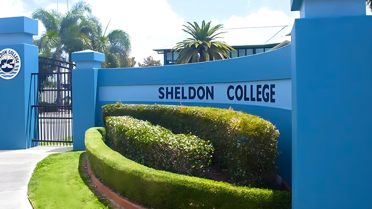Der Eingang des Sheldon College mit blauem Tor und Schild umgeben von Palmen und gepflegten Hecken.