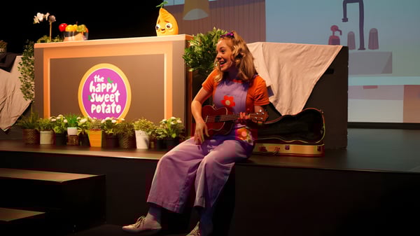 Eine Frau spielt Gitarre auf der Bühne am Sheldon College vor einer Happy Couch Potato Dekoration.