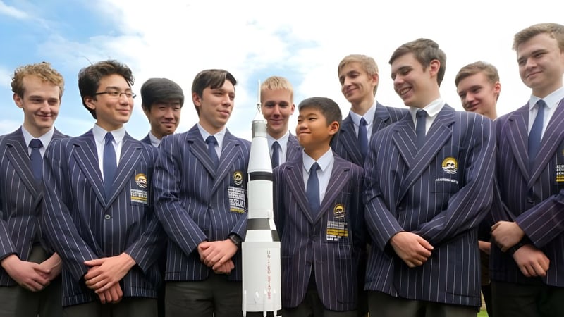 Eine Gruppe junger Männer des Sheldon College steht in dunkelblauen Anzügen zusammen vor einem bewölkten Himmel.