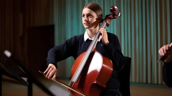 Eine Schülerin der Sherborne Girls' School spielt auf der Bühne ein Cello vor grünen Vorhängen.