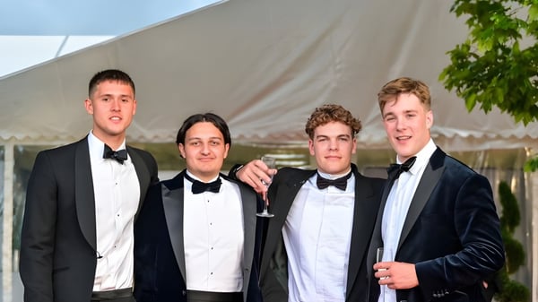 Vier Schüler der Sherborne School in formeller Kleidung posieren zusammen vor einem Zelt und einer grünen Umgebung.