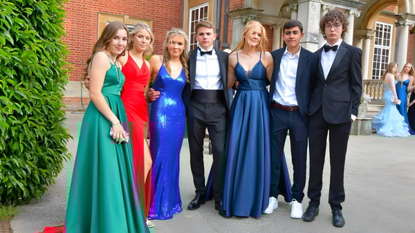 Eine Gruppe elegant gekleideter Personen steht vor dem Backsteingebäude der Sherfield School mit grüner Kulisse.