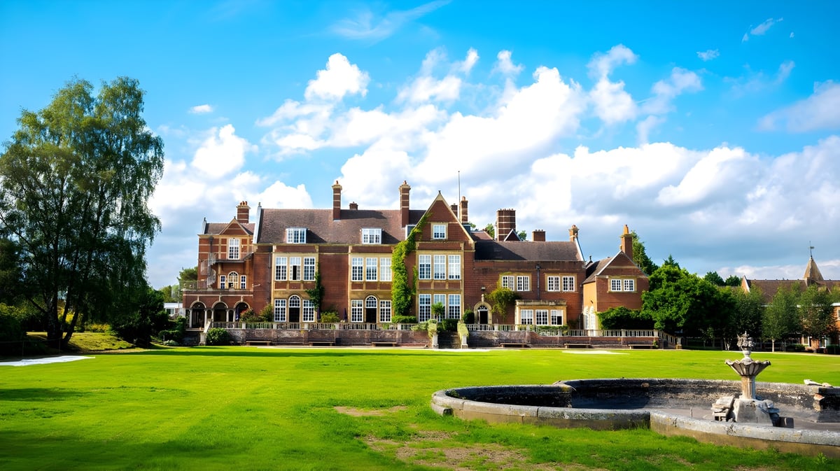 Das eindrucksvolle Backsteingebäude der Sherfield School mit Türmen steht vor einem grünen Rasen und einem Brunnen im Vordergrund.