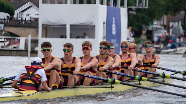 Eine Gruppe von Ruderern in bunten Uniformen sitzt in einem Boot auf dem Wasser auf dem Gelände des Shiplake College.