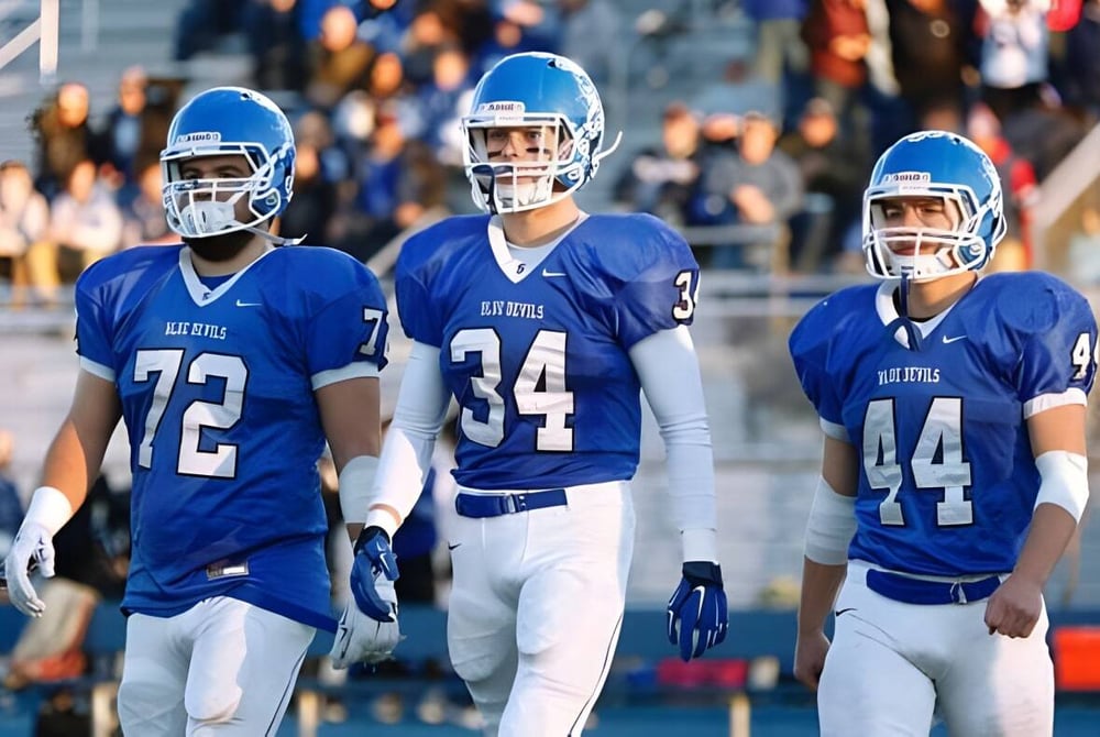 Drei Football-Spieler in blauen Uniformen stehen auf dem Spielfeld der Shore Regional High School vor Zuschauern.