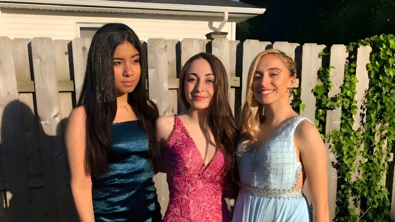 Drei Schülerinnen der Shore Regional High School posieren vor einem Holzzaun mit grüner Vegetation im Hintergrund.