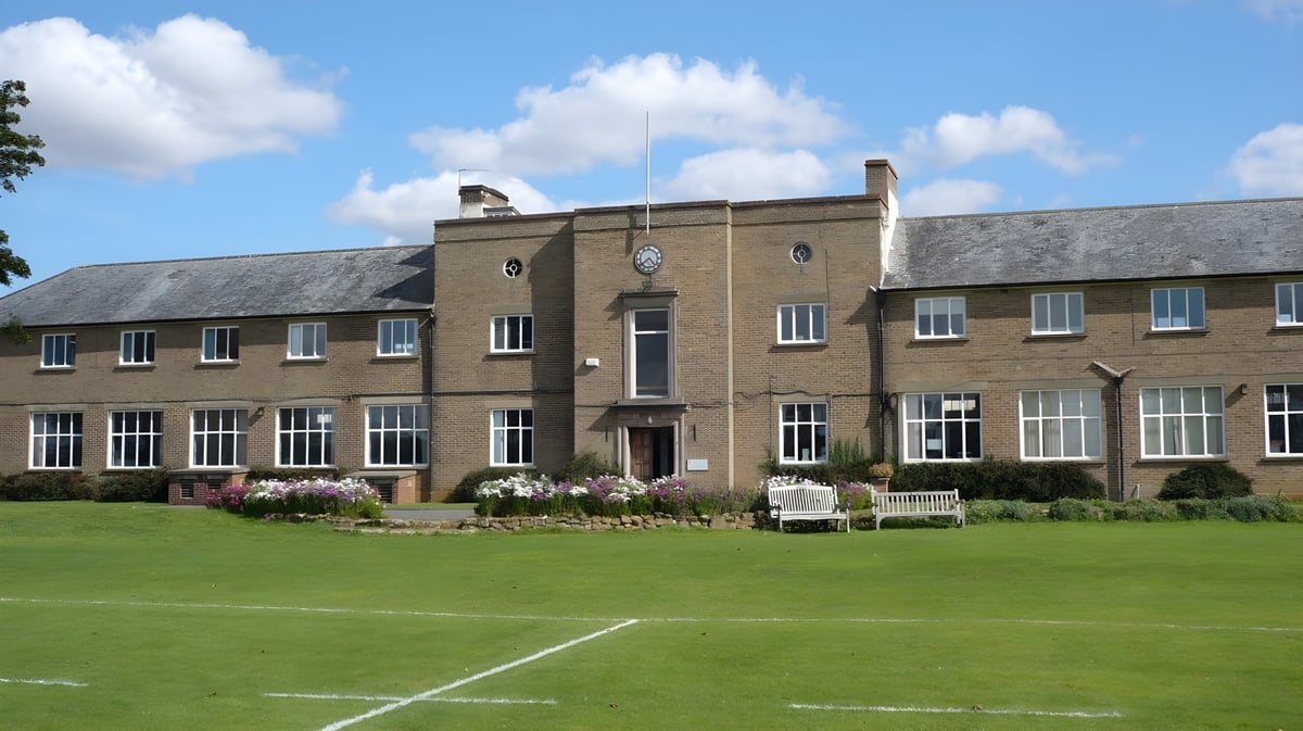 Das Backsteingebäude der Sibford School mit Uhrturm steht hinter einem gepflegten Rasen und Garten.