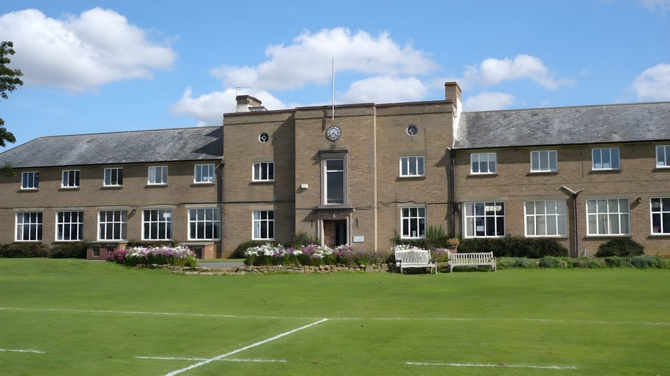 Das große Backsteingebäude mit Uhrturm der Sibford School steht hinter gepflegtem Rasen und Garten.