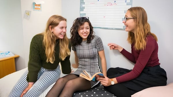 Drei Schülerinnen der Sibford School sitzen zusammen und unterhalten sich in einem Klassenraum mit Whiteboard.