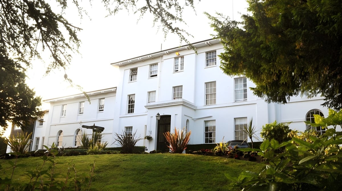 Das weiße Haupthaus der Sidcot School steht vor einem gepflegten Rasen und umgeben von hohen Bäumen.