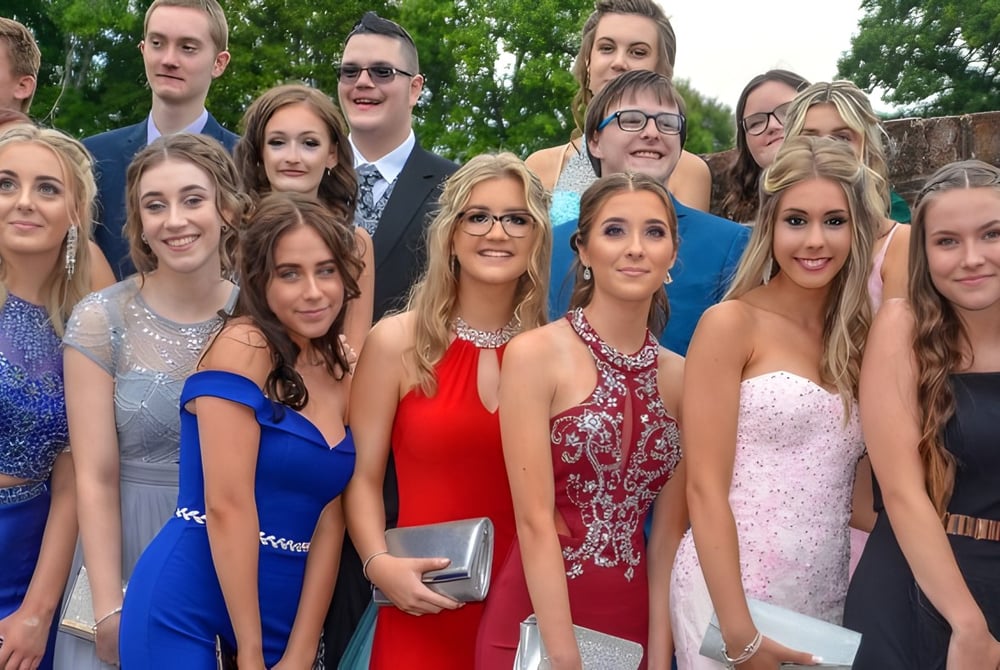 Eine Gruppe junger Menschen in formeller Kleidung posiert draußen vor Bäumen auf dem Gelände der Sidcot School.
