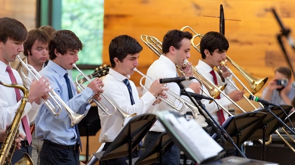 Eine Gruppe junger Musiker der Sidwell Friends School spielt Blechblasinstrumente auf einer Bühne vor einem Holzhintergrund.