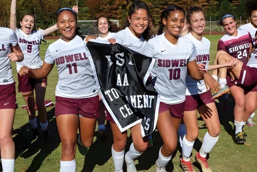 Eine Gruppe junger Fußballspielerinnen der Sidwell Friends School versammelt sich lächelnd auf einem grasbewachsenen Spielfeld mit Bäumen im Hintergrund.