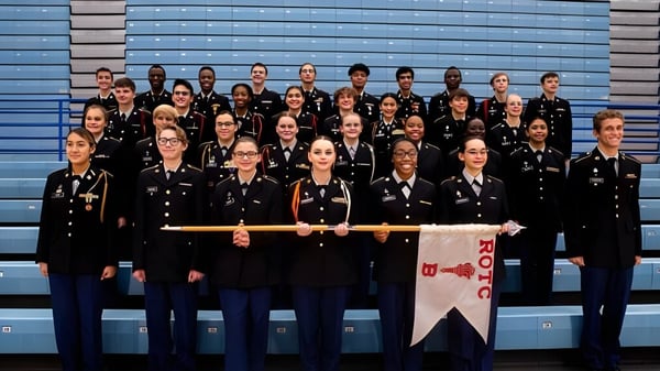 Eine Gruppe Schüler des Sierra Vista Unified School District steht mit schwarzen Uniformen vor blau-grauem Hintergrund und hält ein Banner.