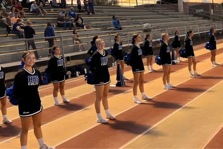 Eine Gruppe Cheerleader des Sierra Vista Unified School District steht in Formation auf einem Basketballfeld mit Zuschauern im Hintergrund.