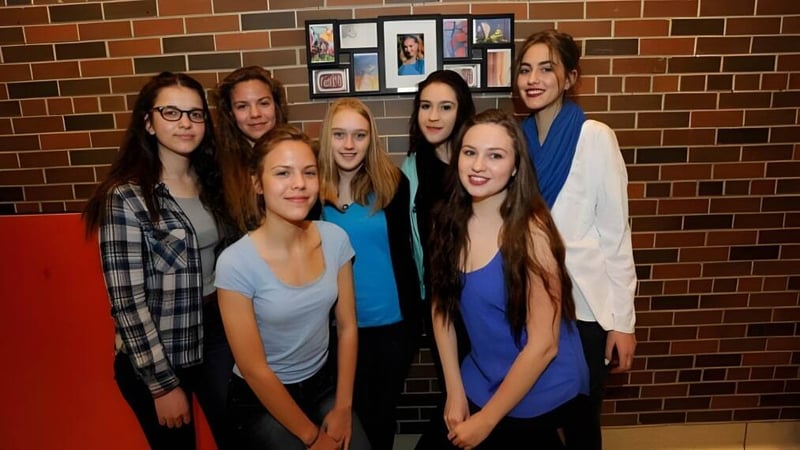 Eine Gruppe Schülerinnen steht vor einer Backsteinwand mit gerahmten Fotos auf dem Campus der Silverthorn Collegiate Institute.