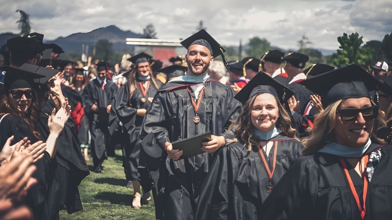 Eine Gruppe von Absolventen der Simpson University trägt schwarze Abschlussroben und Hüte bei einer Abschlussfeier im Freien.