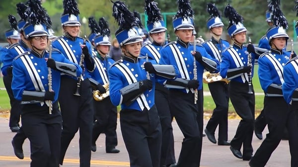 Mitglieder der Marching Band der Sioux Falls Christian School stehen in blauer und schwarzer Uniform auf einem Rasen mit Bäumen im Hintergrund.