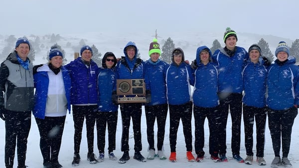 Eine Gruppe von Schülerinnen und Schülern der Sioux Falls Christian School steht in blauen und grauen Wintersportuniformen vor einer verschneiten Berglandschaft.