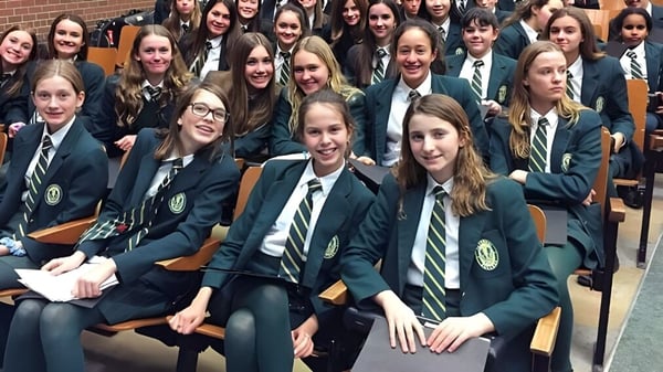 Eine Gruppe von Schülerinnen und Schülern in Schuluniform sitzt in Reihen und lächelt in die Kamera auf dem Campus des Sir John A. Macdonald Collegiate Institute.