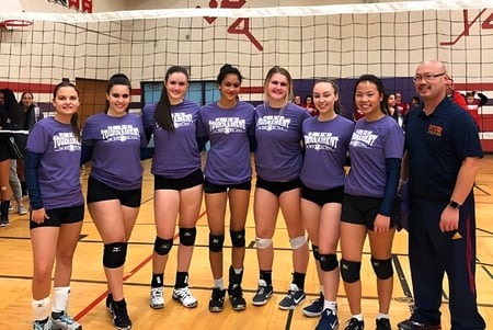 Eine Gruppe weiblicher Volleyballspielerinnen in lila Uniformen steht auf dem Volleyballfeld des Sir John A. Macdonald Collegiate Institute.