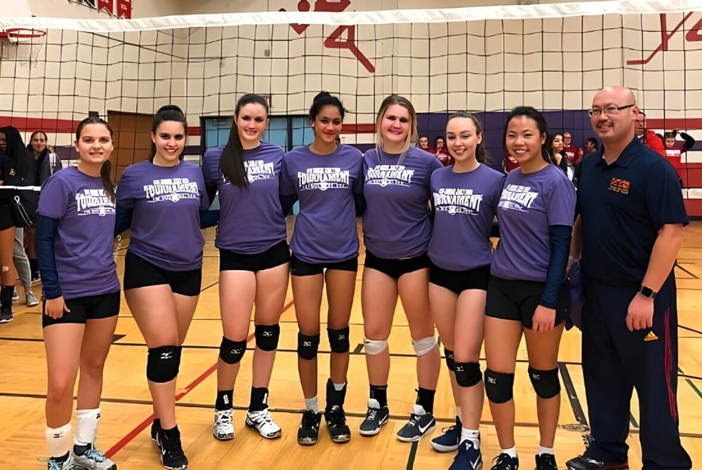 Eine Gruppe weiblicher Volleyballspielerinnen in lila Uniformen steht auf dem Volleyballfeld des Sir John A. Macdonald Collegiate Institute.