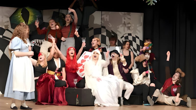 Schüler der Sir Wilfred Laurier Secondary School treten in bunten Kostümen auf einer Bühne mit kariertem Hintergrund auf.