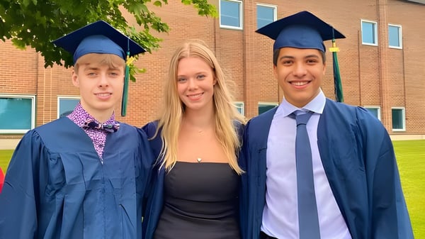 Drei Schülerinnen und Schüler der Sir Wilfred Laurier Secondary School feiern ihren Abschluss vor einem Backsteingebäude.