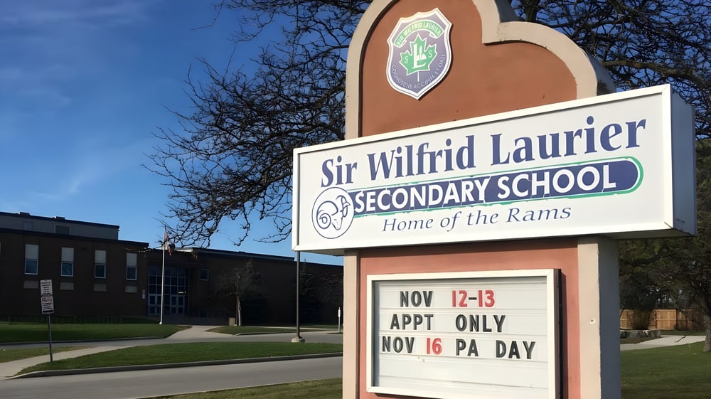 Das Schild der Sir Wilfrid Laurier Secondary School zeigt Informationen zu Terminen vor einem Hintergrund aus Bäumen und blauem Himmel.